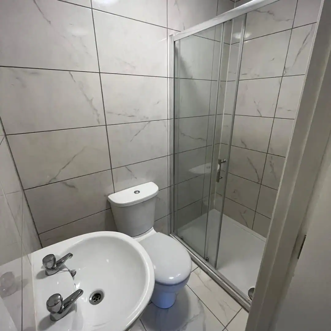 Bathroom with white marble effect tiles, toilet, sink, and glass shower in Dublin 7 flat. – Ghar.ie property listing