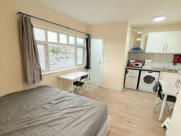 Studio apartment in Bray, Co. Wicklow, featuring a bed, table, kitchenette, and washing machine. – Ghar.ie property listing