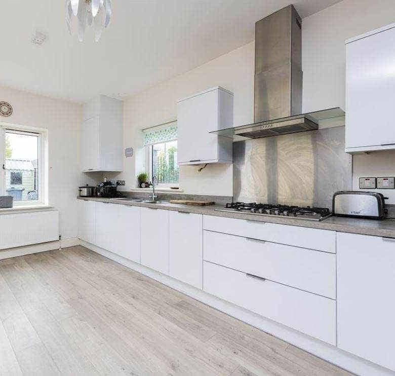 Bright kitchen with white cabinets, light wood floors, and a window, showcasing modern design. – Ghar.ie property listing