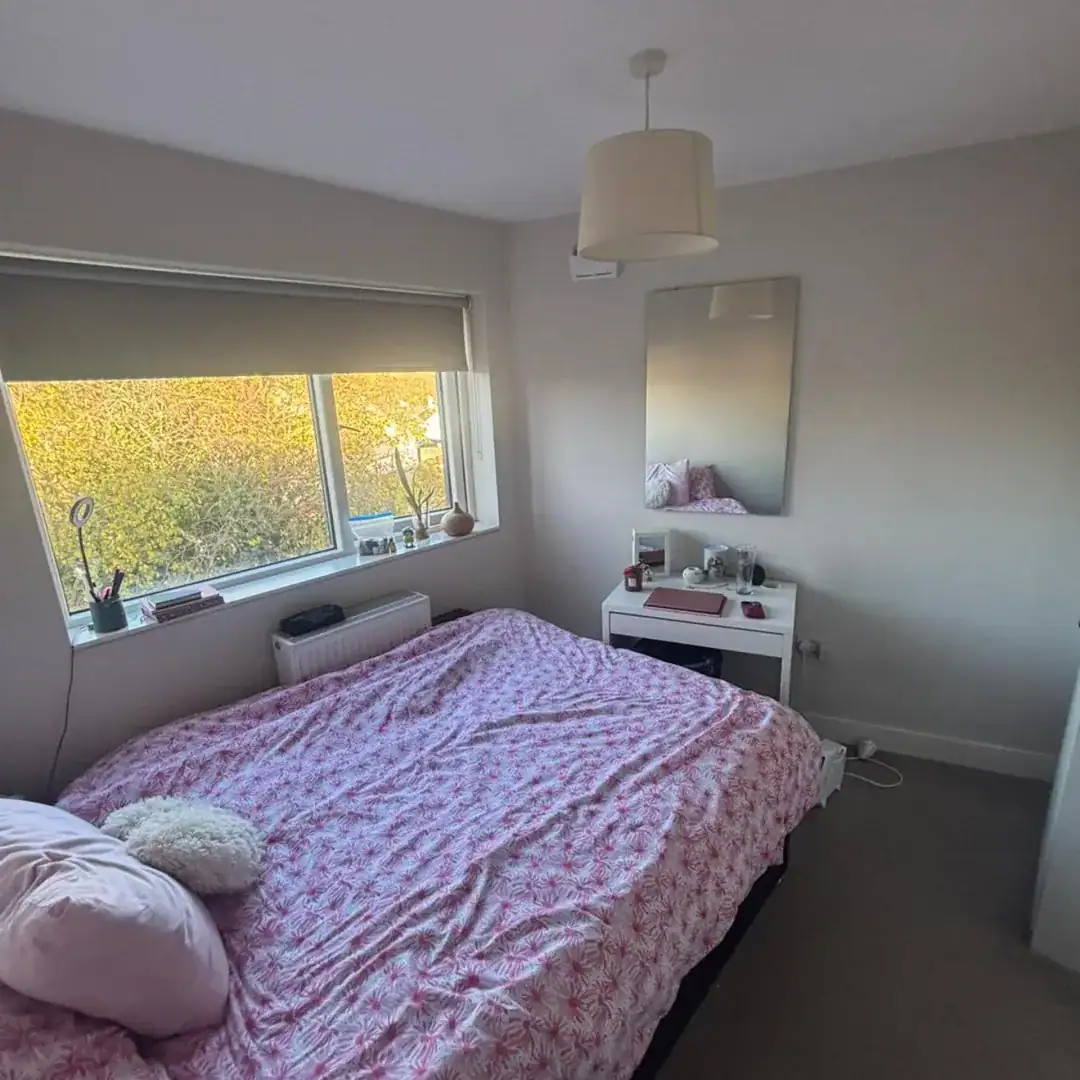 Bedroom featuring a double bed with pink floral bedding, mirror, and window in Blanchardstown, D15. – Ghar.ie property listing