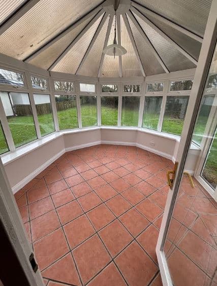 Bright sunroom with terracotta tile floor and large windows overlooking green lawn.