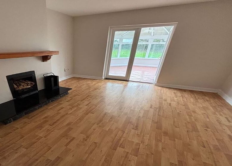 Living room with fireplace, wood floors, and sliding doors to a sunroom. Neutral wall colors.