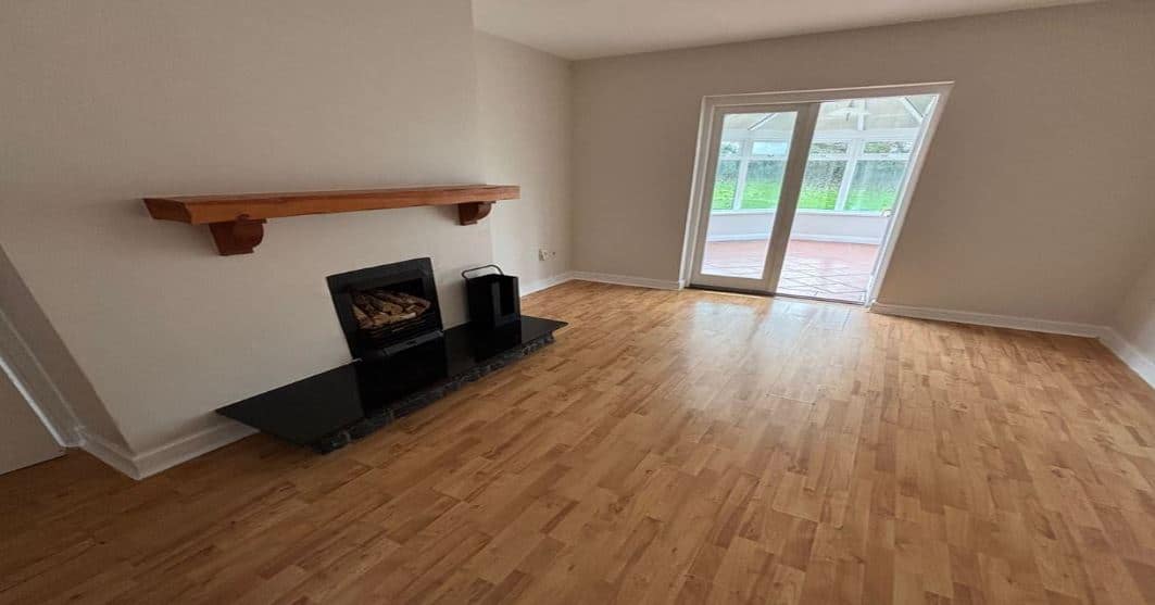 Living room with fireplace, wood floors, and sliding doors to a sunroom. Neutral wall colors.