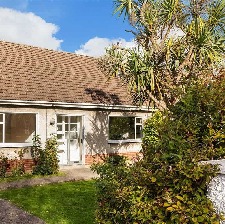 Charming single-story house with brown roof, small lawn, and palm tree in the front yard.