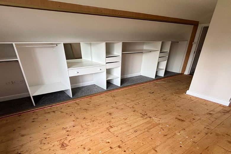 White built-in wardrobe with shelves and hanging space in a bedroom.