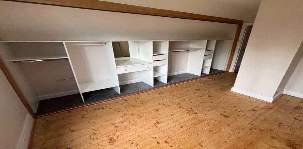 White built-in wardrobe with shelves and hanging space in a bedroom.