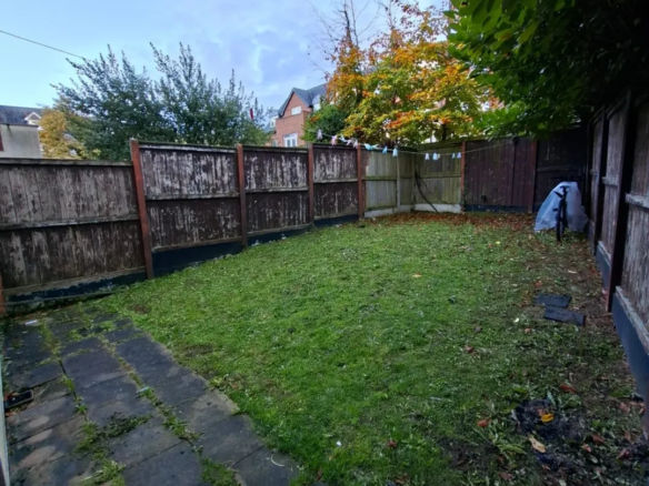 Backyard garden with grass, wooden fence, and patio. Autumn leaves visible.