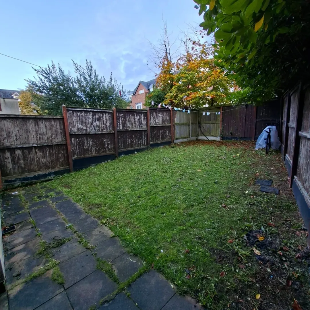 Backyard garden with grass, wooden fence, and patio. Autumn leaves visible.