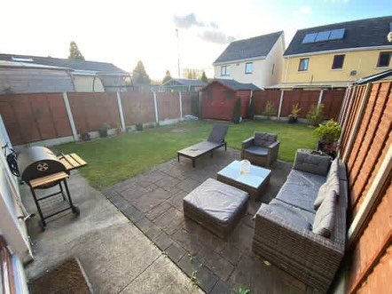 Backyard patio with wicker furniture, grill, and lawn.