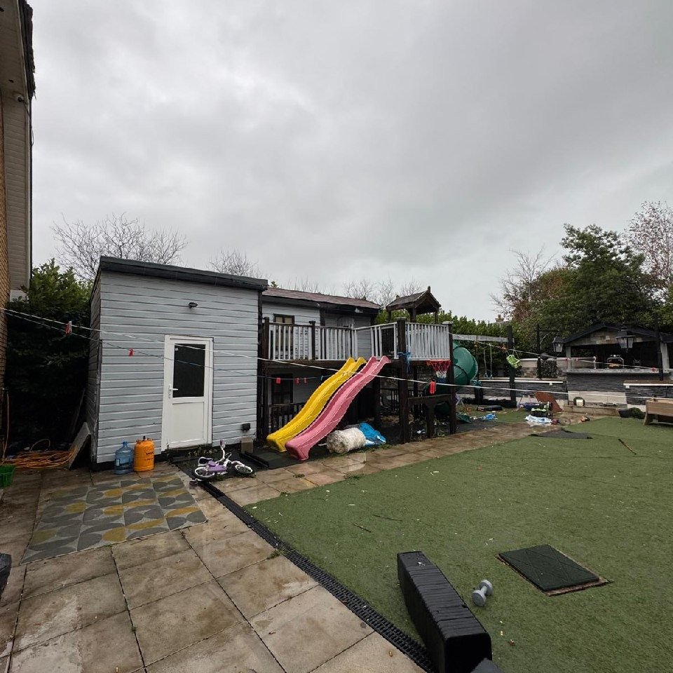 Backyard play area with slides, playhouse, and artificial grass on a cloudy day.
