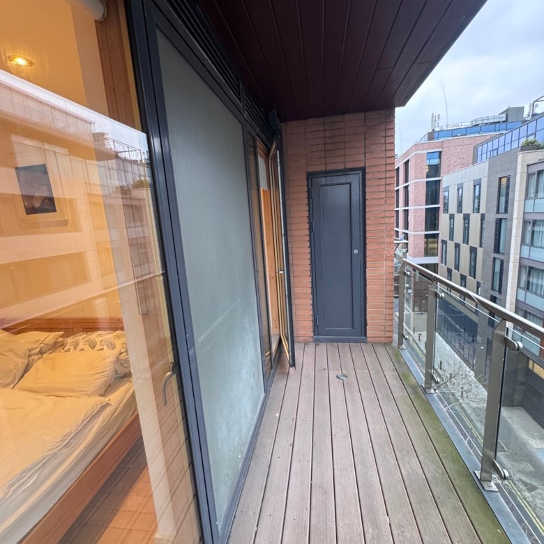 Balcony view with wood decking, brick wall, and building reflection.