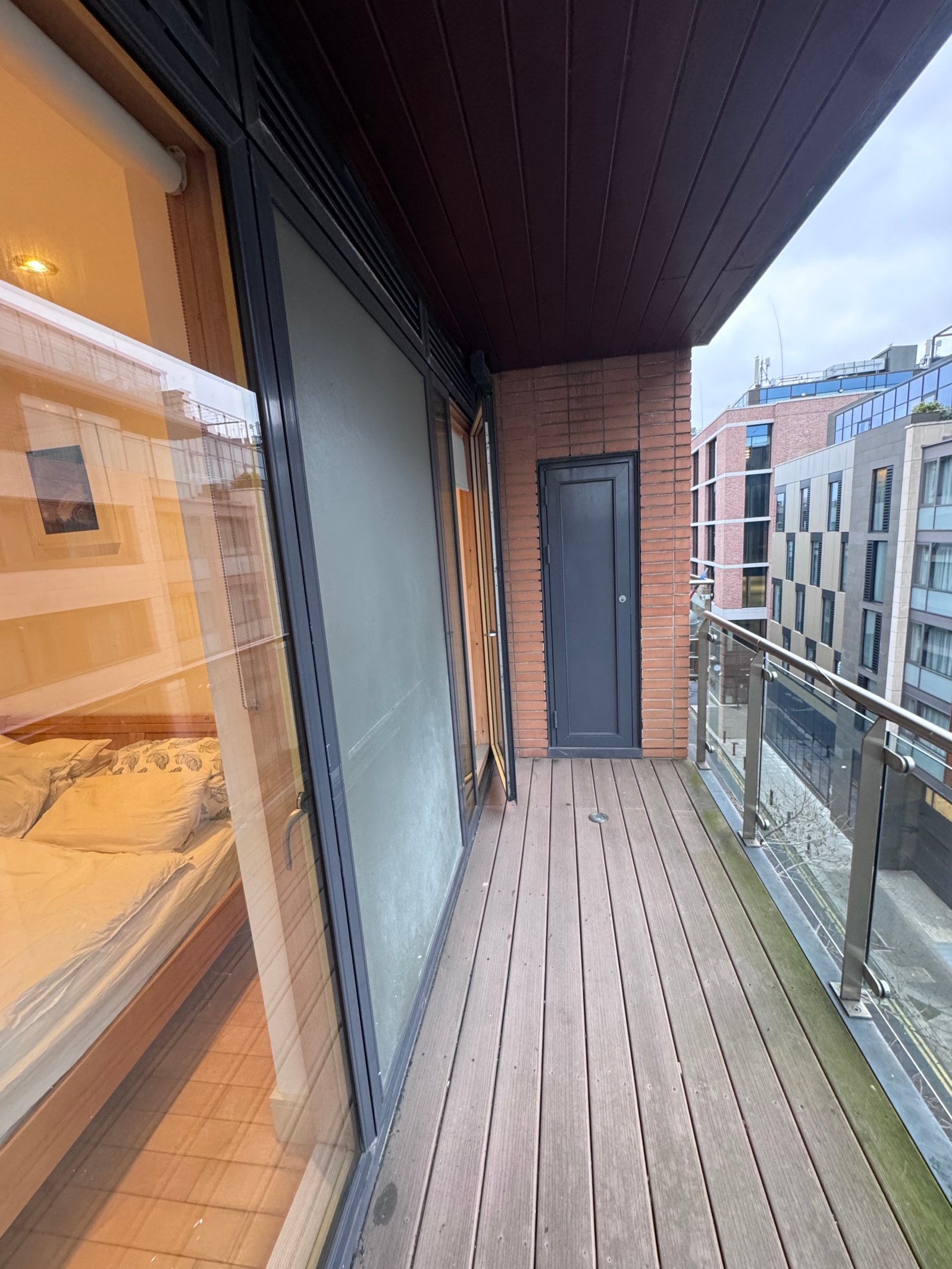 Balcony view with wood decking, brick wall, and building reflection.