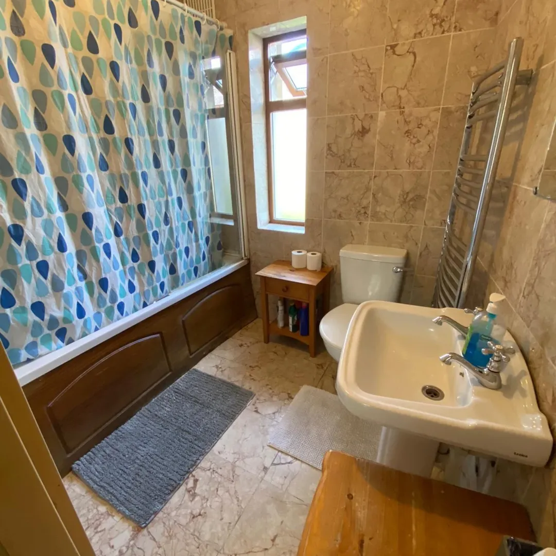 Bathroom with blue shower curtain, pedestal sink, and marble tile.