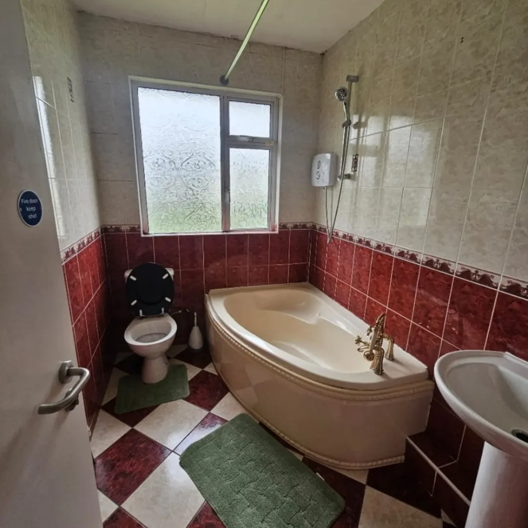 Corner bathtub, toilet, and sink in a bathroom with red and beige tile.