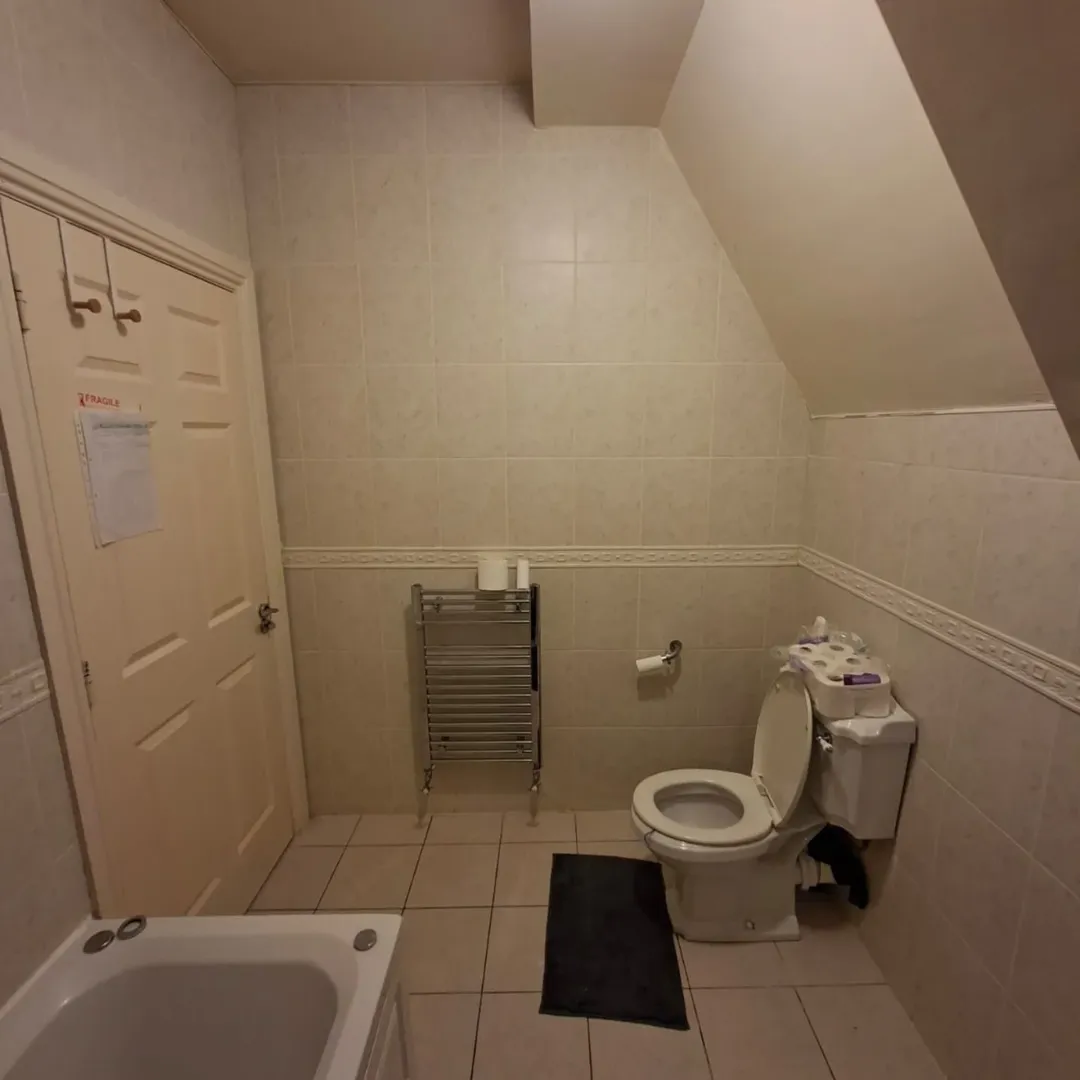 Bathroom with toilet, towel rack, and bathtub under an angled ceiling.