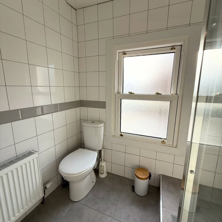Bathroom with toilet, window, radiator, and gray tile.