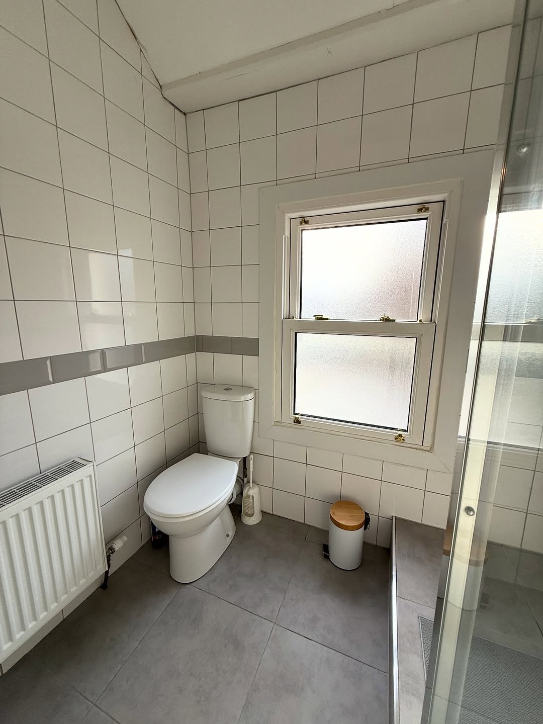 Bathroom with toilet, window, and radiator against tiled walls.