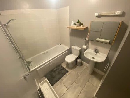 Bathroom with tub, toilet, sink, and cabinet. Neutral color scheme.