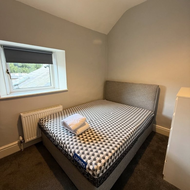 Bedroom with bed, window, and radiator. Towels are neatly folded on the bed.