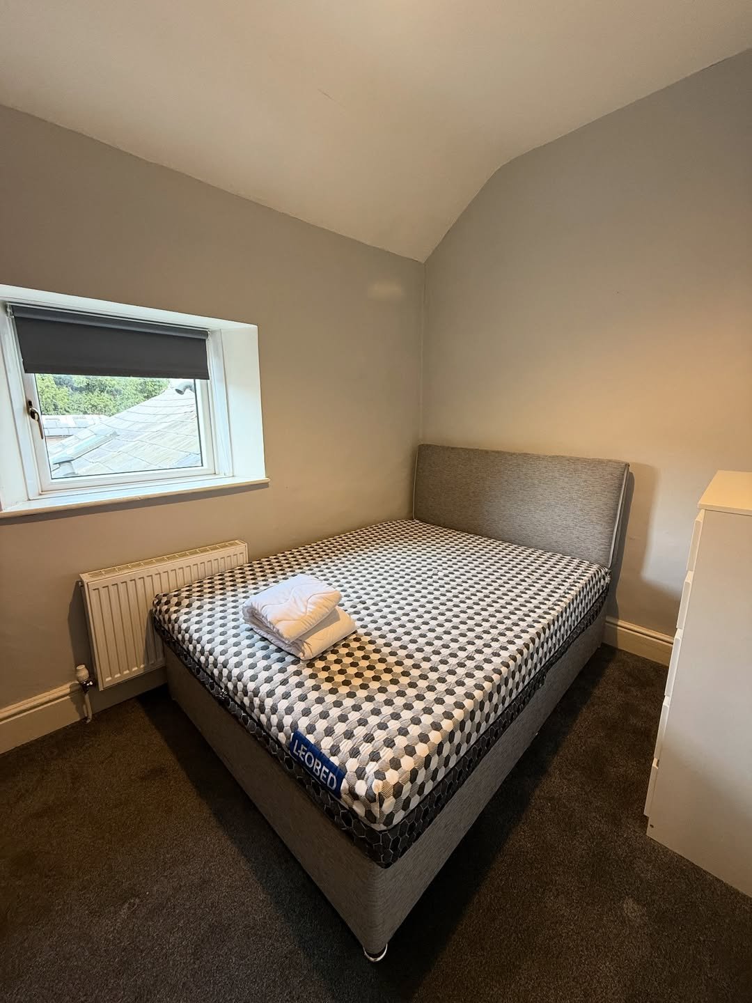 Bedroom with bed, window, and radiator. Towels are neatly folded on the bed.
