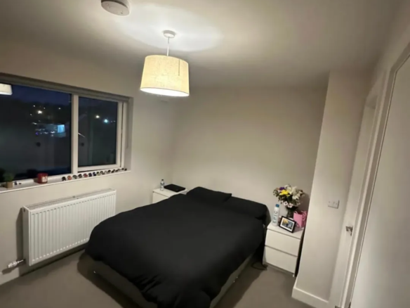 Cozy bedroom with black bedding, white nightstands, and soft lighting.