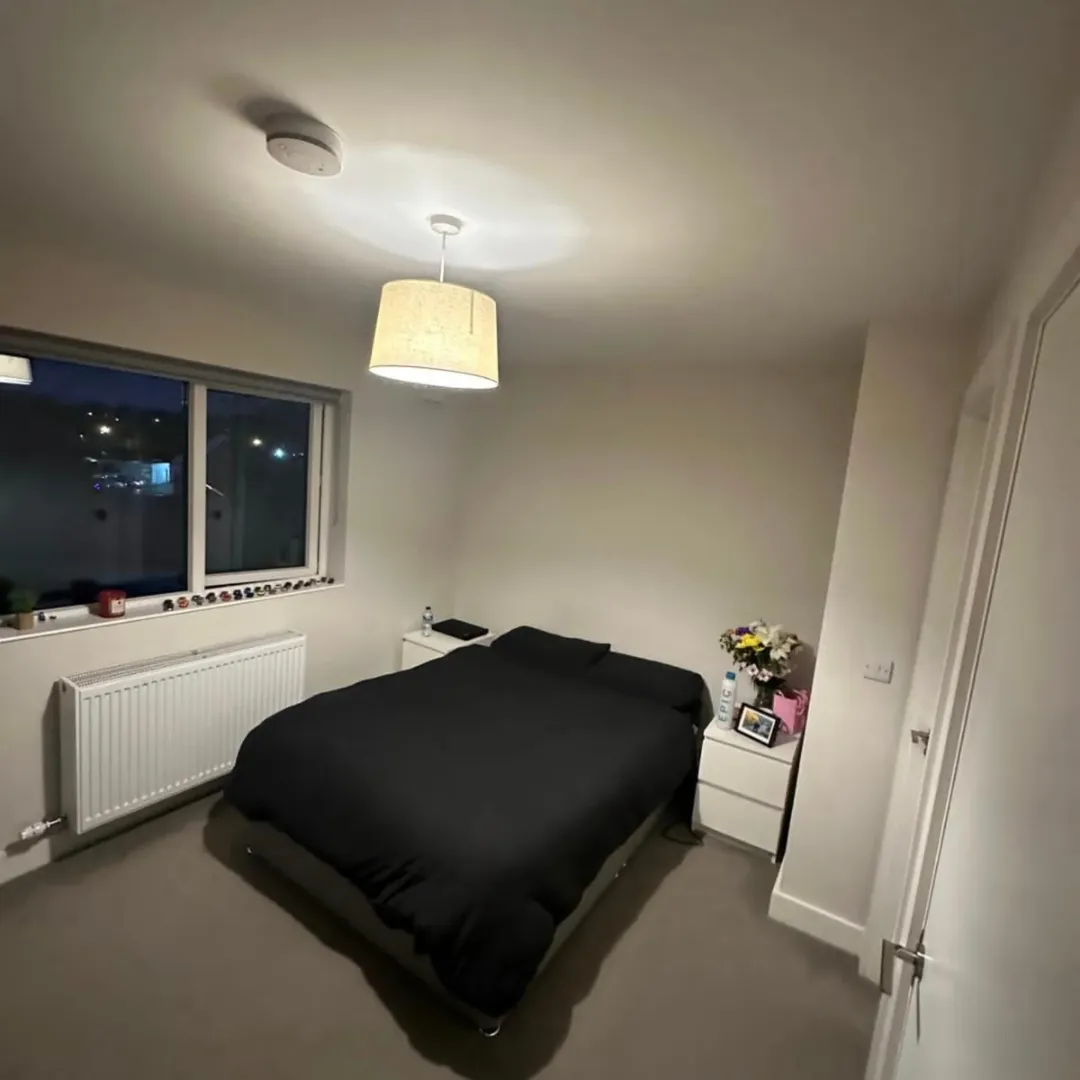 Cozy bedroom with black bedding, white nightstands, and soft lighting.