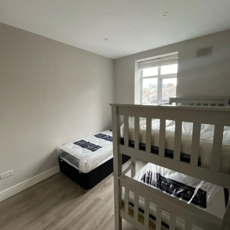 Bedroom with bunk bed and single bed, neutral walls and wood floor.