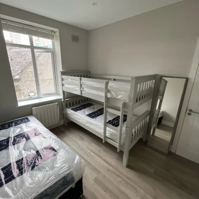 Bedroom with bunk beds, single bed, mirror, and window.