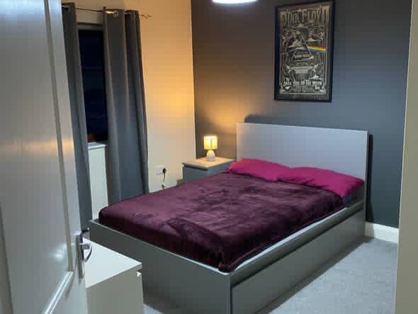 Bedroom with gray bed, nightstand lamp, and Pink Floyd poster.