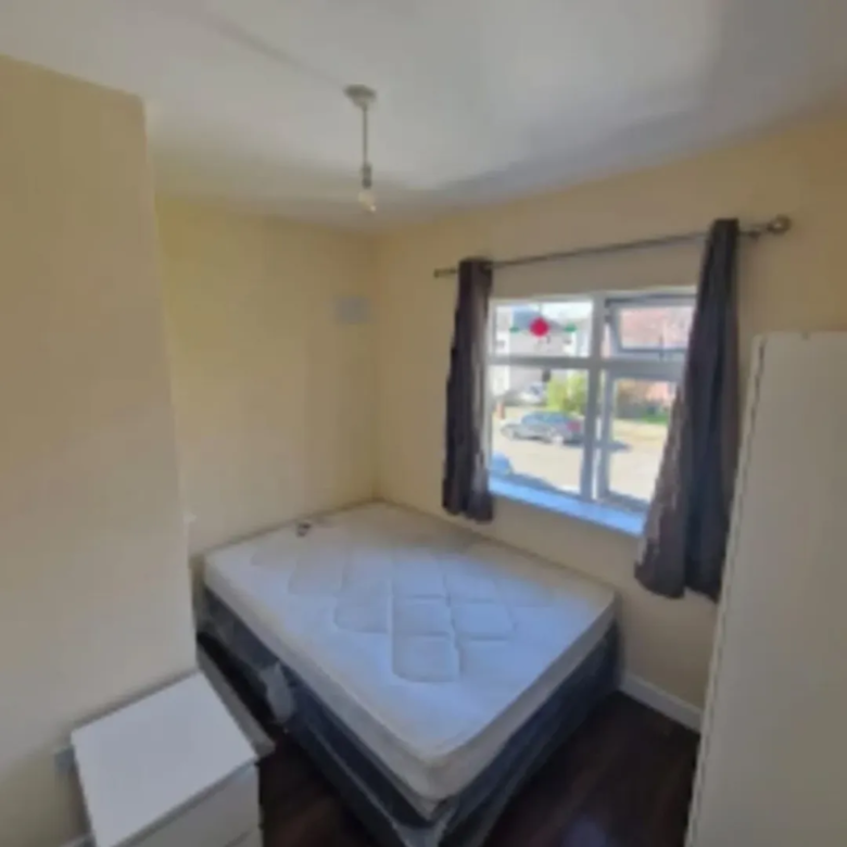 Bedroom interior with bed, window, curtains, nightstand, and wardrobe. Neutral walls and dark wood floor.