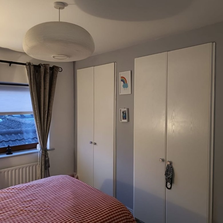 Bedroom interior: red and white bed, white closets, curtained window, and modern light fixture.