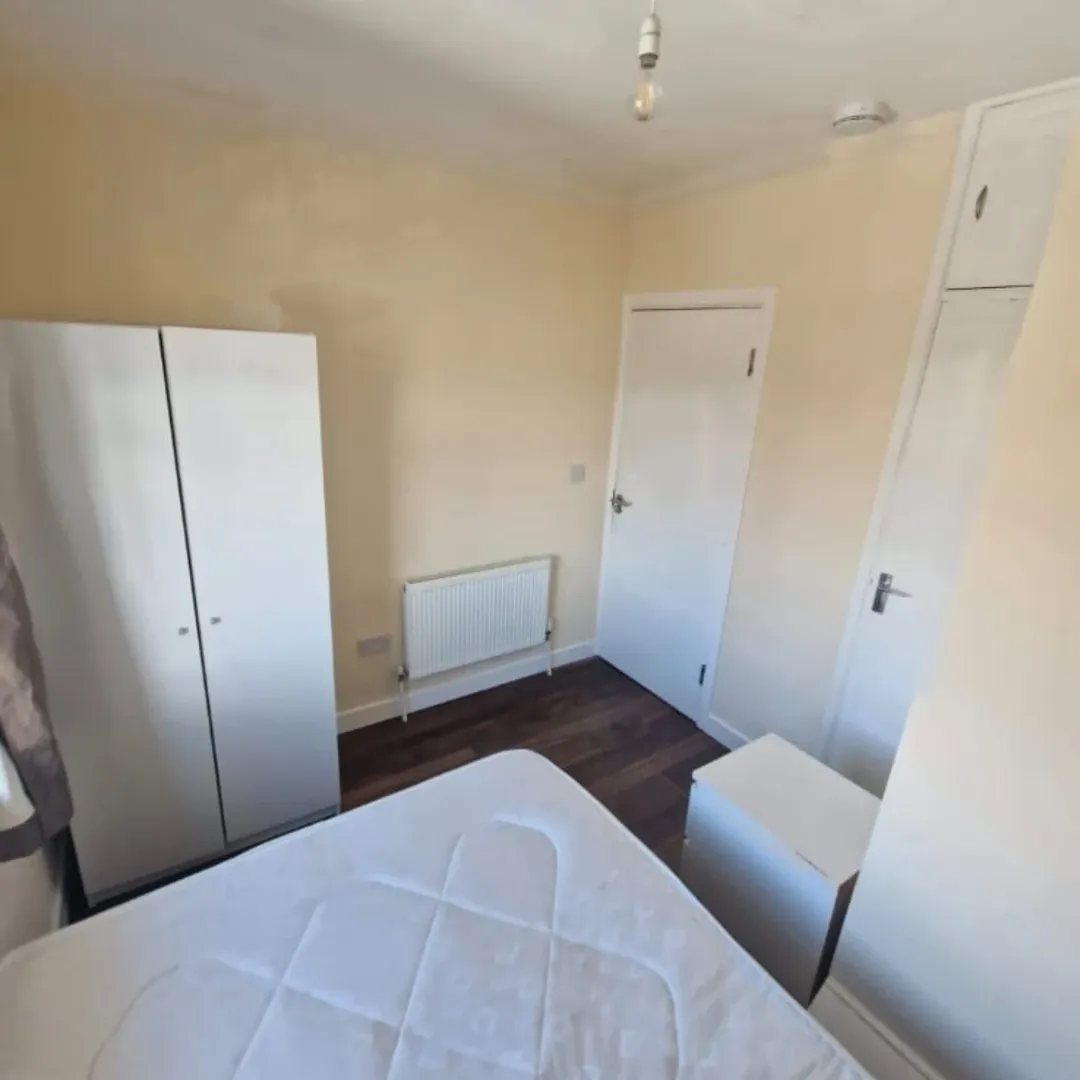 Bedroom interior with white furniture, radiator, and dark wood flooring.