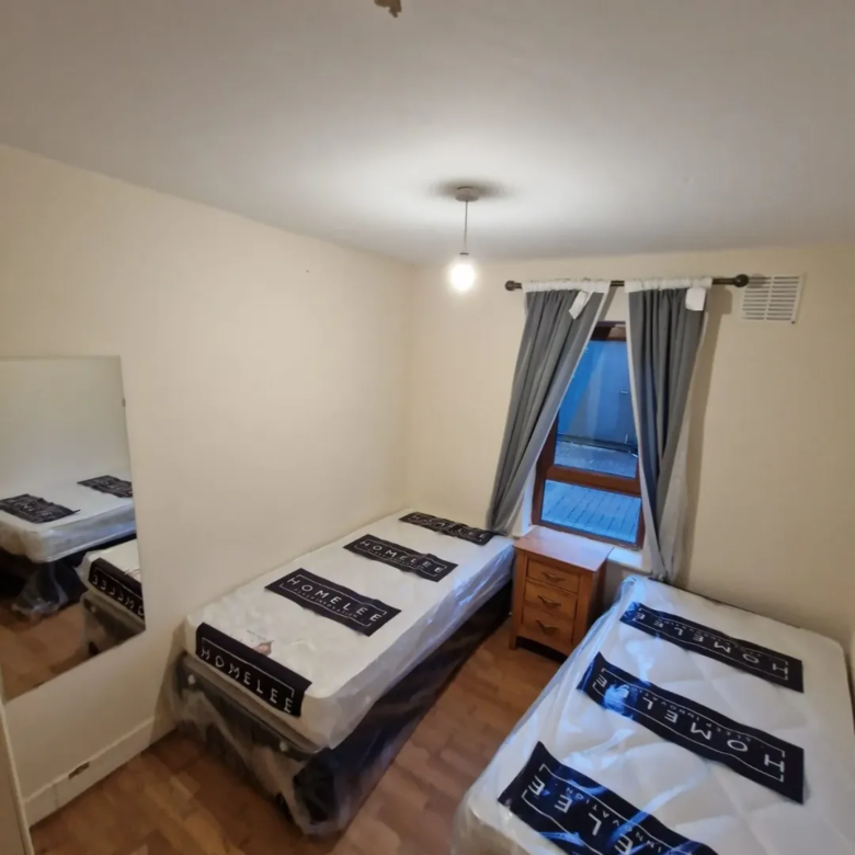 Bedroom with two twin beds, nightstand, mirror, and window with gray curtains.