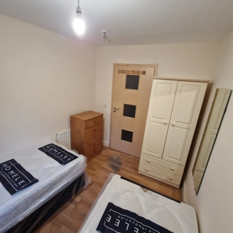 Bedroom with two beds, wardrobe, chest of drawers, and mirror.