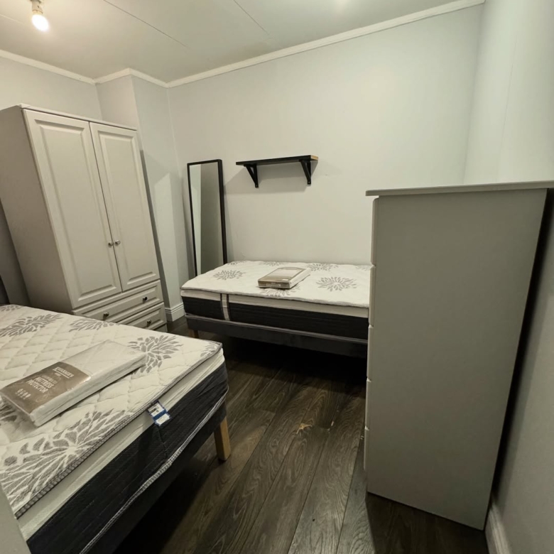 Bedroom with two beds, wardrobe, chest of drawers, and mirror.