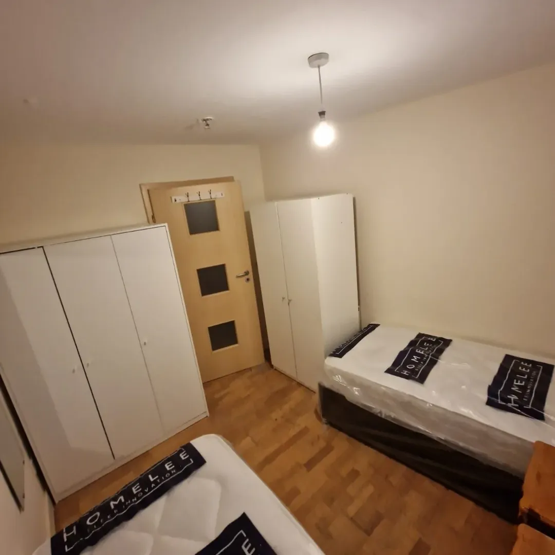 Bedroom with two beds, wardrobes, and wooden floor. HOMELEE logo visible.