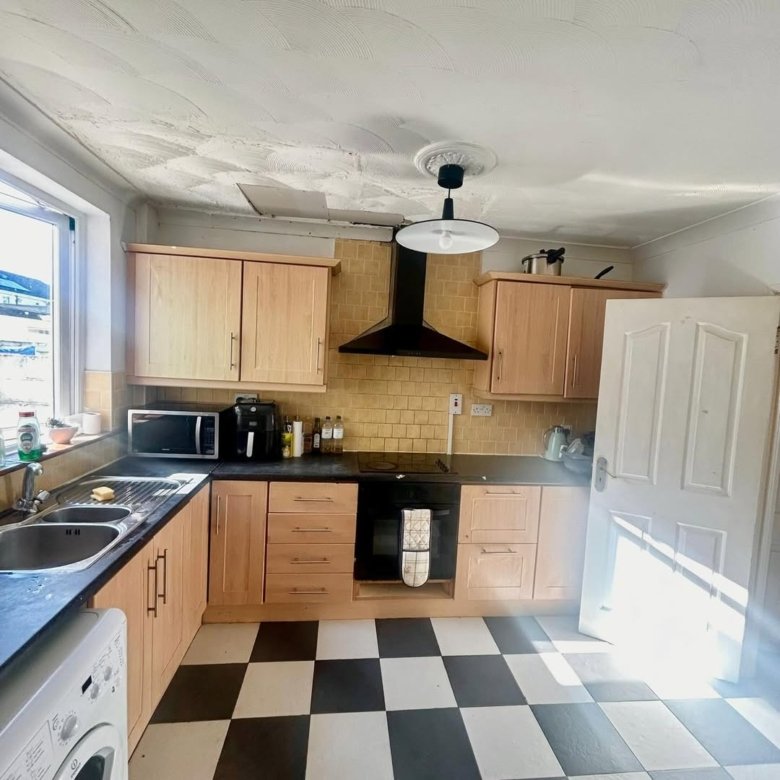 Bright kitchen with black and white checkered floor, light wood cabinets, and black appliances.