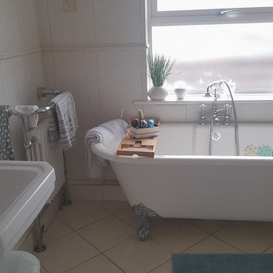Clawfoot bathtub with bath tray, towels, and plants in bright bathroom.