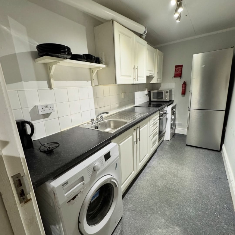 Compact kitchen with white cabinets, black countertop, stainless steel fridge, and washing machine.
