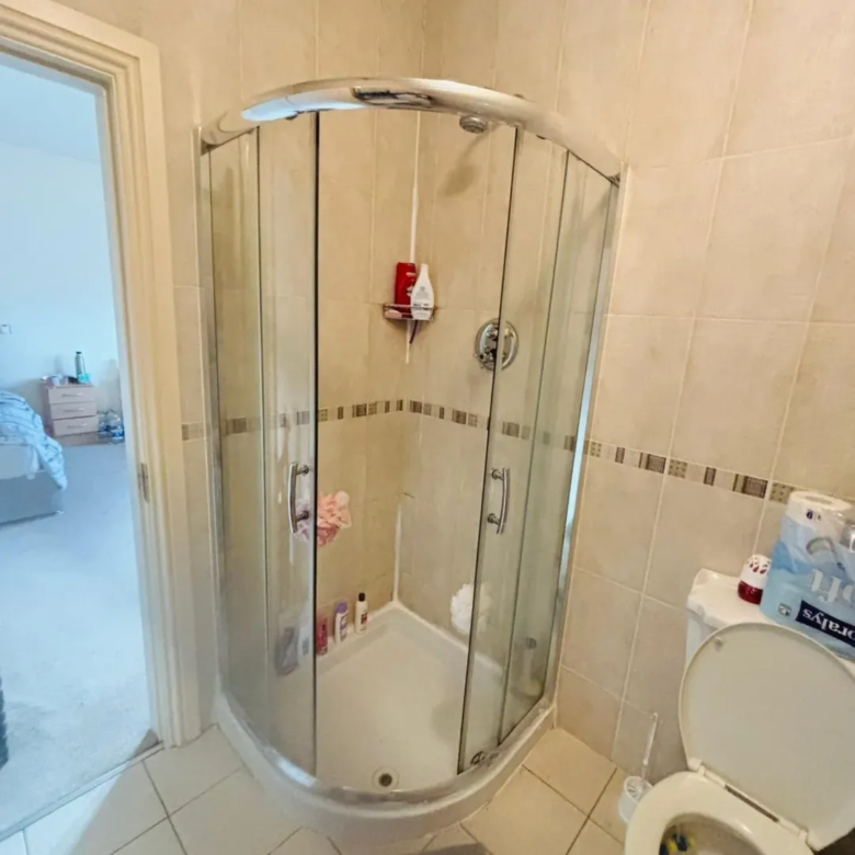 Corner shower unit in tiled bathroom, toilet visible.