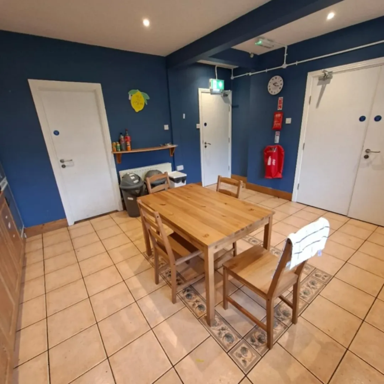 Dining area with wood table, chairs, tile floor, and blue walls in a communal space.