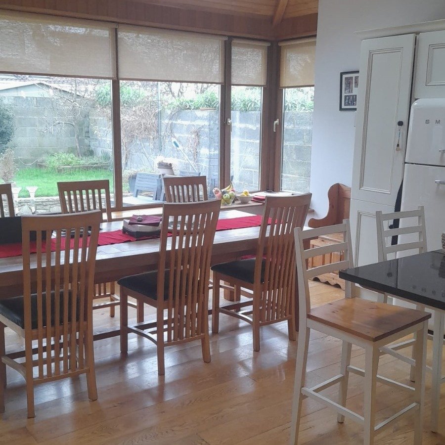 Dining room with wood table, chairs, and view to garden through windows.