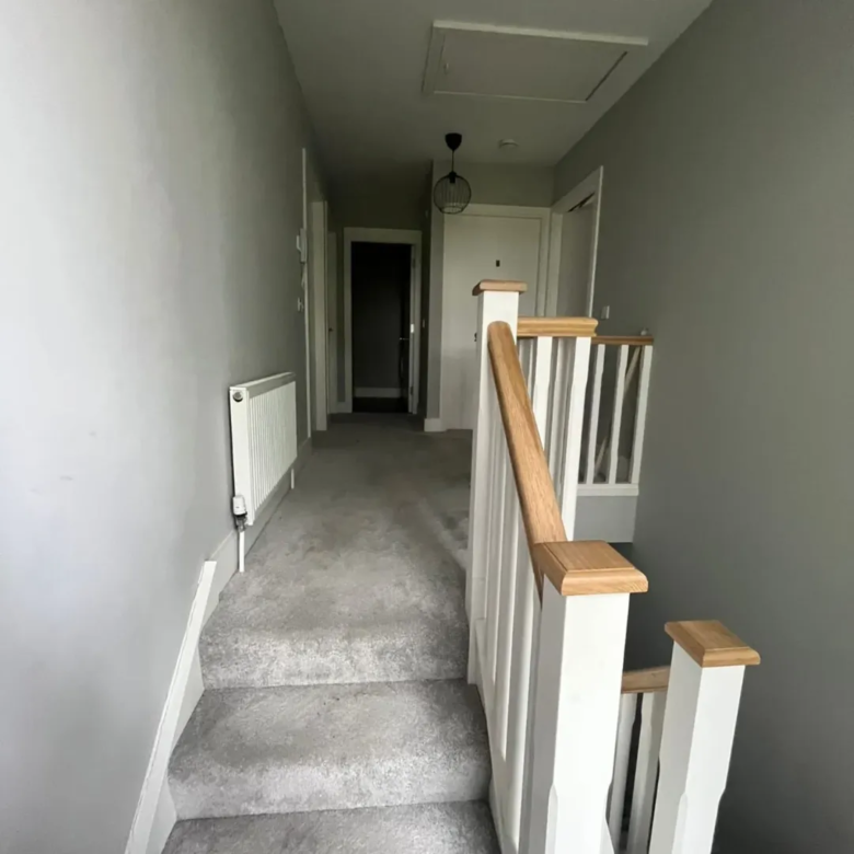Hallway with gray carpet, white banister, and radiator along wall.