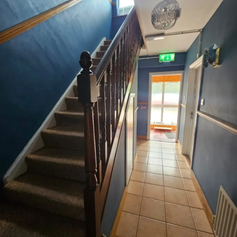Hallway with staircase, blue walls, and tiled floor. Exit sign visible.