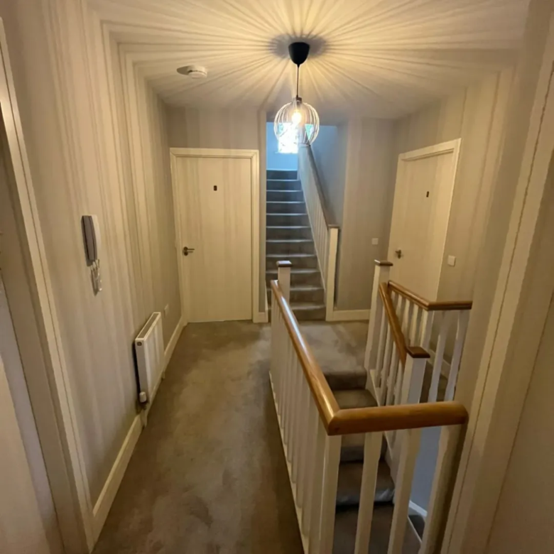 Hallway with stairs, doors, carpet, modern light fixture, and white and wood banister.