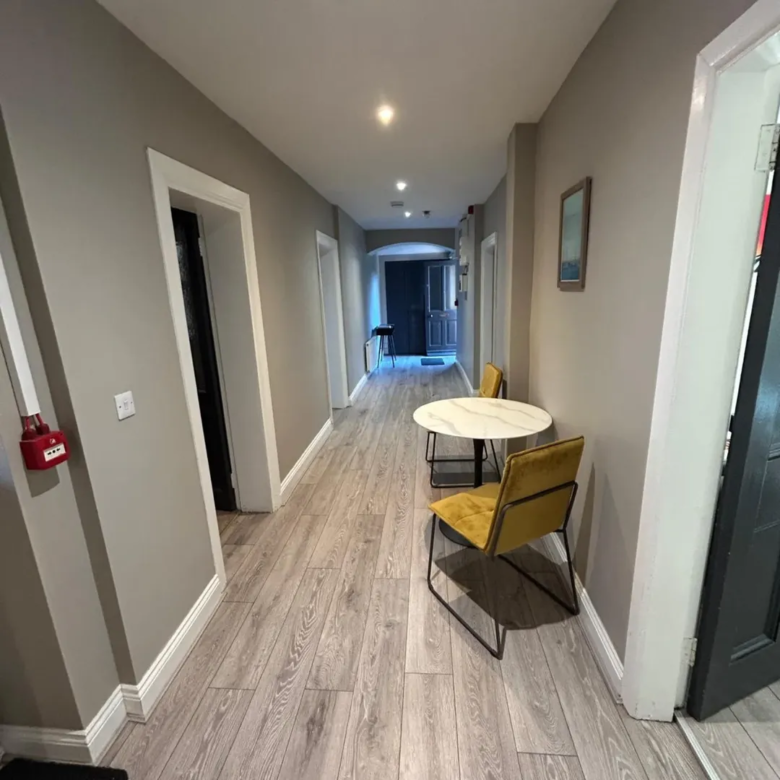 Hallway with table and chairs, grey walls, and light wood flooring.