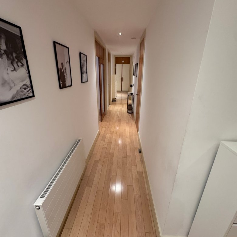 Hallway with wood floors and white walls decorated with framed photos.