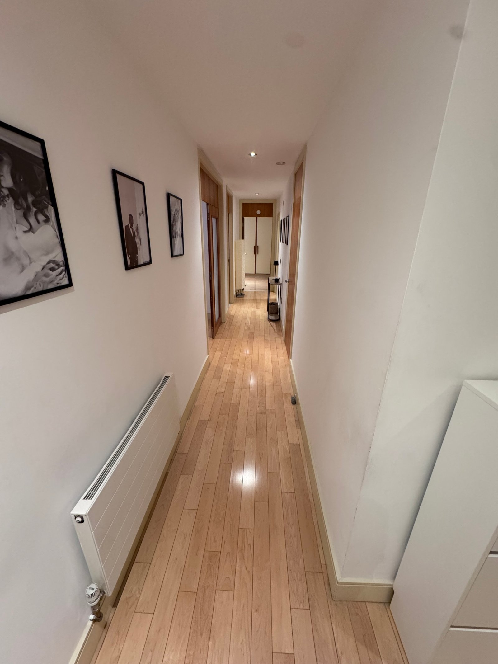 Hallway with wood floors and white walls decorated with framed photos.