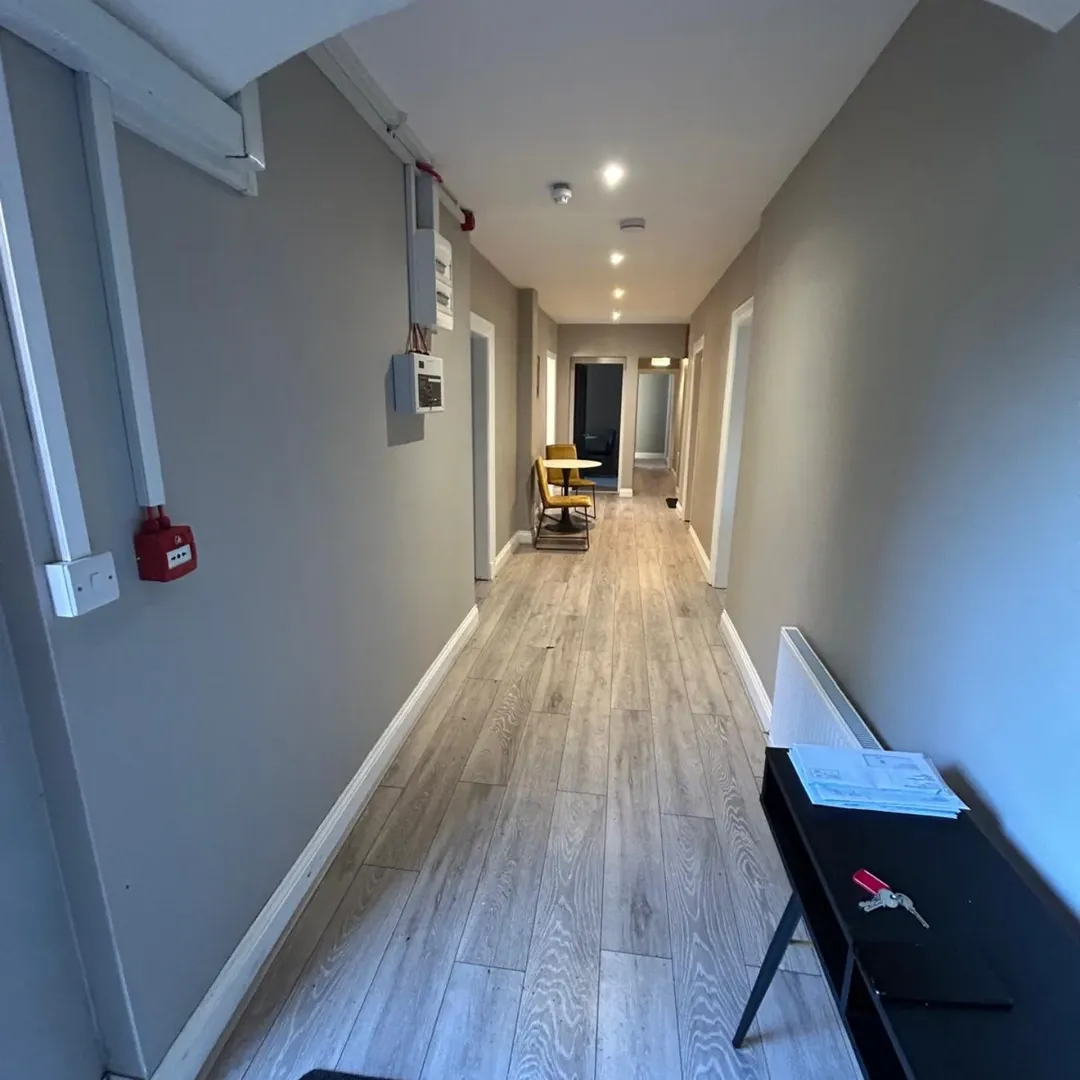 Hallway interior with gray walls, light wood floors, and a table and chairs in the distance.