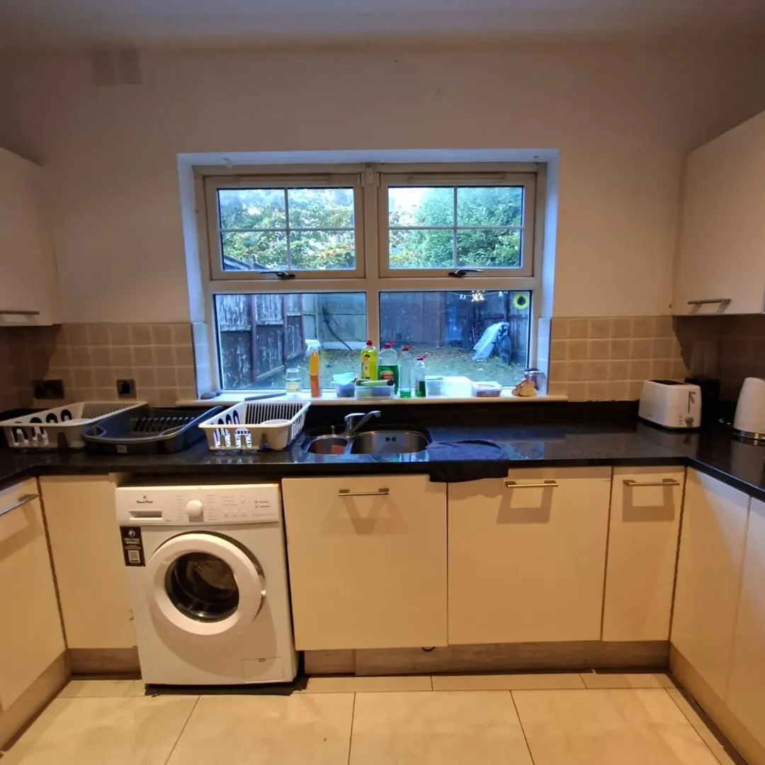 Kitchen with washing machine, sink, and window overlooking a garden.